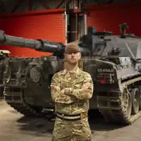 A man in uniform stands with his arms crossed in front of a tank.