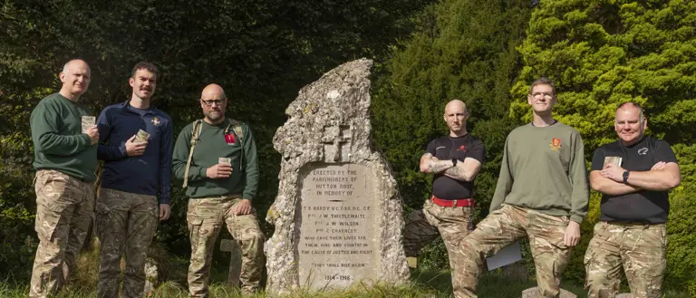 Six soldiers wearing camouflage trousers and a jumper, stand and pose for a photo at the end of their charity walk but a stone memorial plaque.