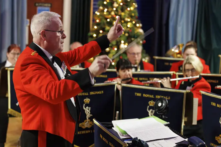 Conductor in a red jacket leading The Royal Signals band during a festive performance.