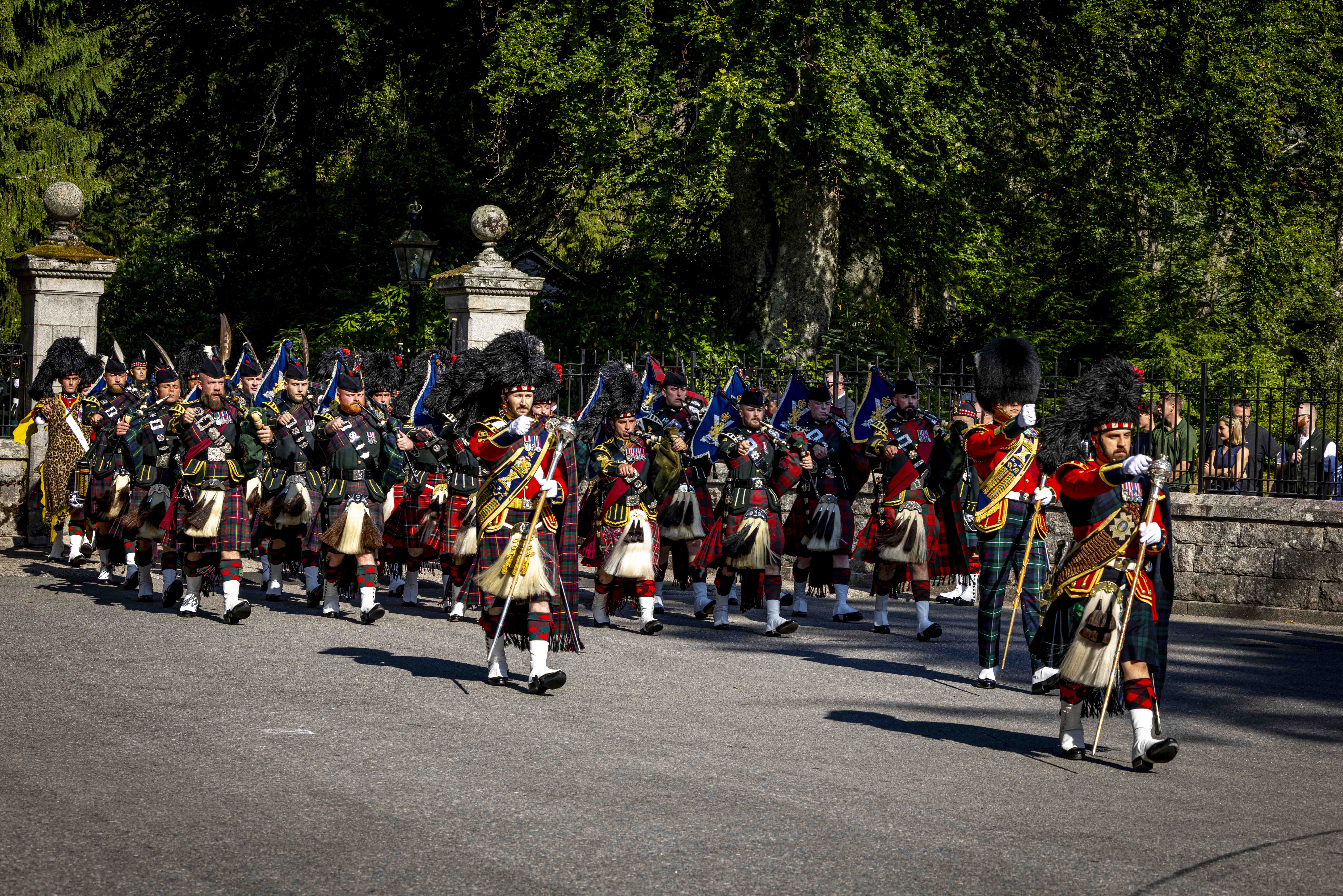 A Scottish pipe band in traditional tartan kilts march in formation on a sunny day.