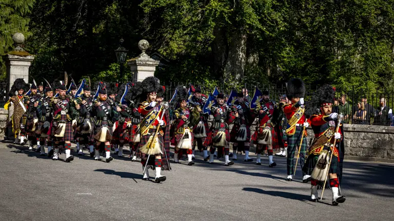 A Scottish pipe band in traditional tartan kilts march in formation on a sunny day.