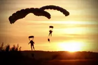 Two soldiers parachute with a sunset behind them.