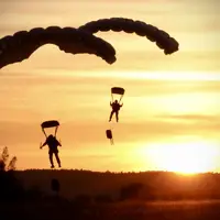 Two soldiers parachute with a sunset behind them.