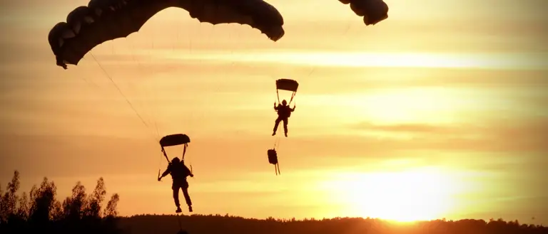 Two soldiers parachute with a sunset behind them.