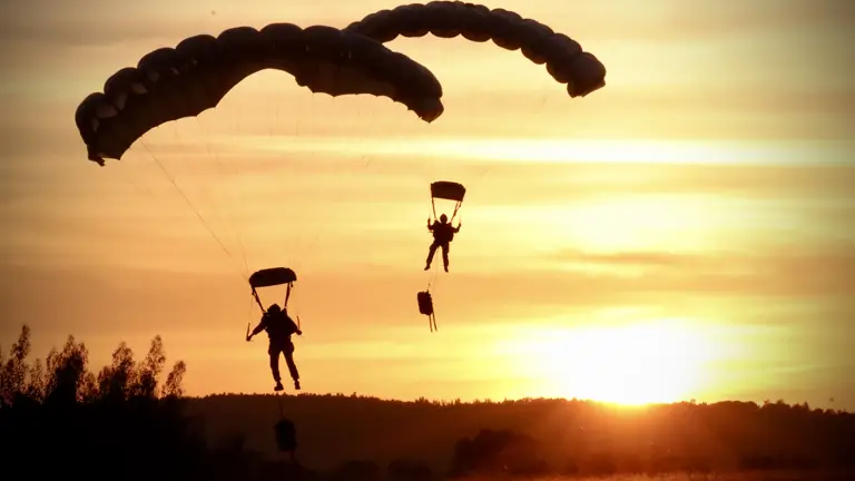 Two soldiers parachute with a sunset behind them.