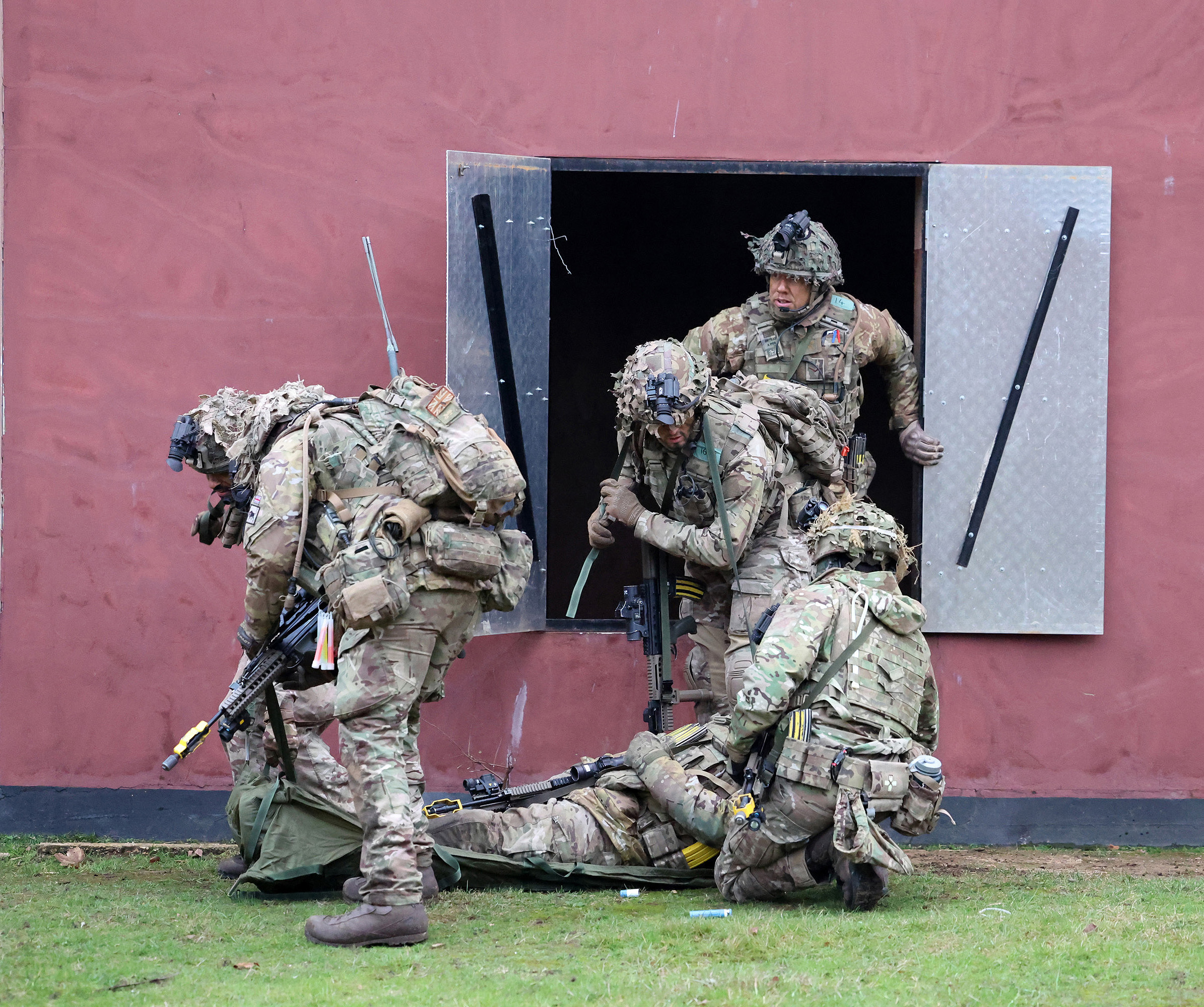 Soldiers wearing camouflage uniforms climb out of a window and prepare to move a casualty.