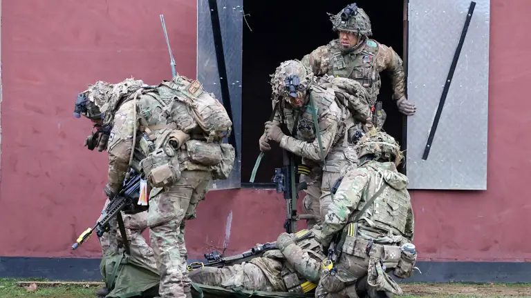 Soldiers wearing camouflage uniforms climb out of a window and prepare to move a casualty.