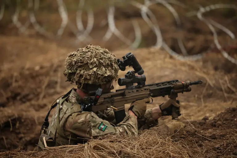 A man is pictured firing an assault rifle from a trench.