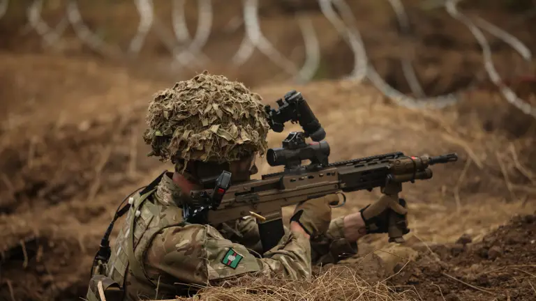 A man is pictured firing an assault rifle from a trench.