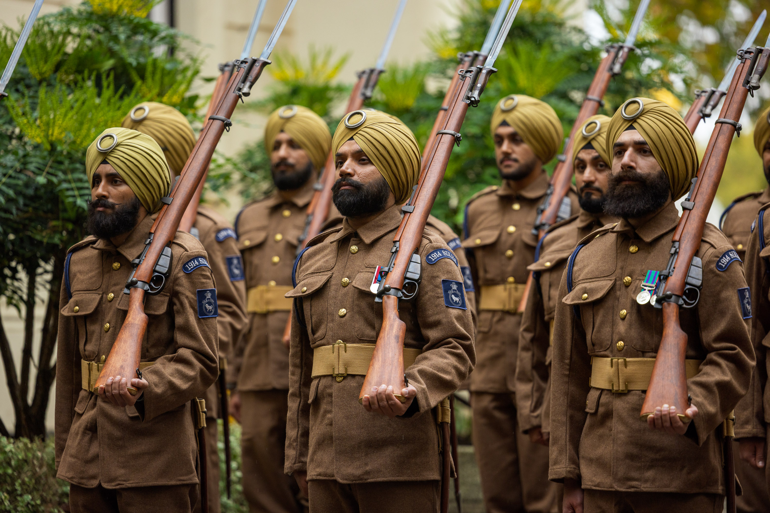 Soldiers in brown uniforms and yellow turbans stand in formation holding rifles with bayonets attached.
