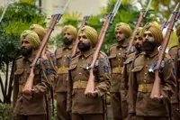 Soldiers in brown uniforms and yellow turbans stand in formation holding rifles with bayonets attached.