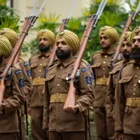 Soldiers in brown uniforms and yellow turbans stand in formation holding rifles with bayonets attached.