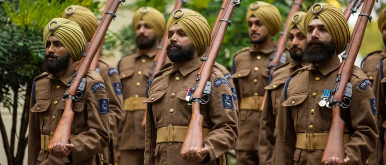 Soldiers in brown uniforms and yellow turbans stand in formation holding rifles with bayonets attached.