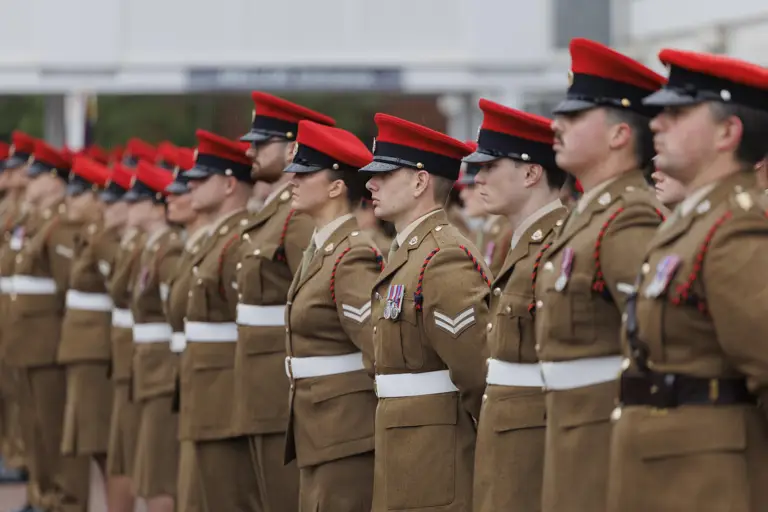 Soldiers stood in line next to each other wearing their brown smart uniforms with red caps on their heads.