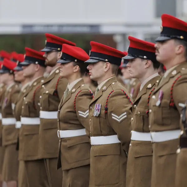 Soldiers stood in line next to each other wearing their brown smart uniforms with red caps on their heads.