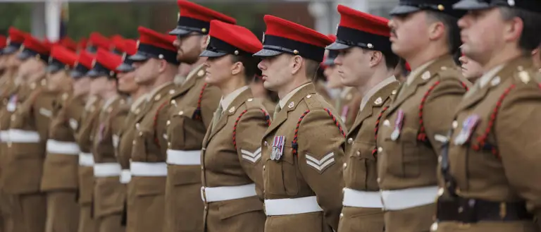 Soldiers stood in line next to each other wearing their brown smart uniforms with red caps on their heads.