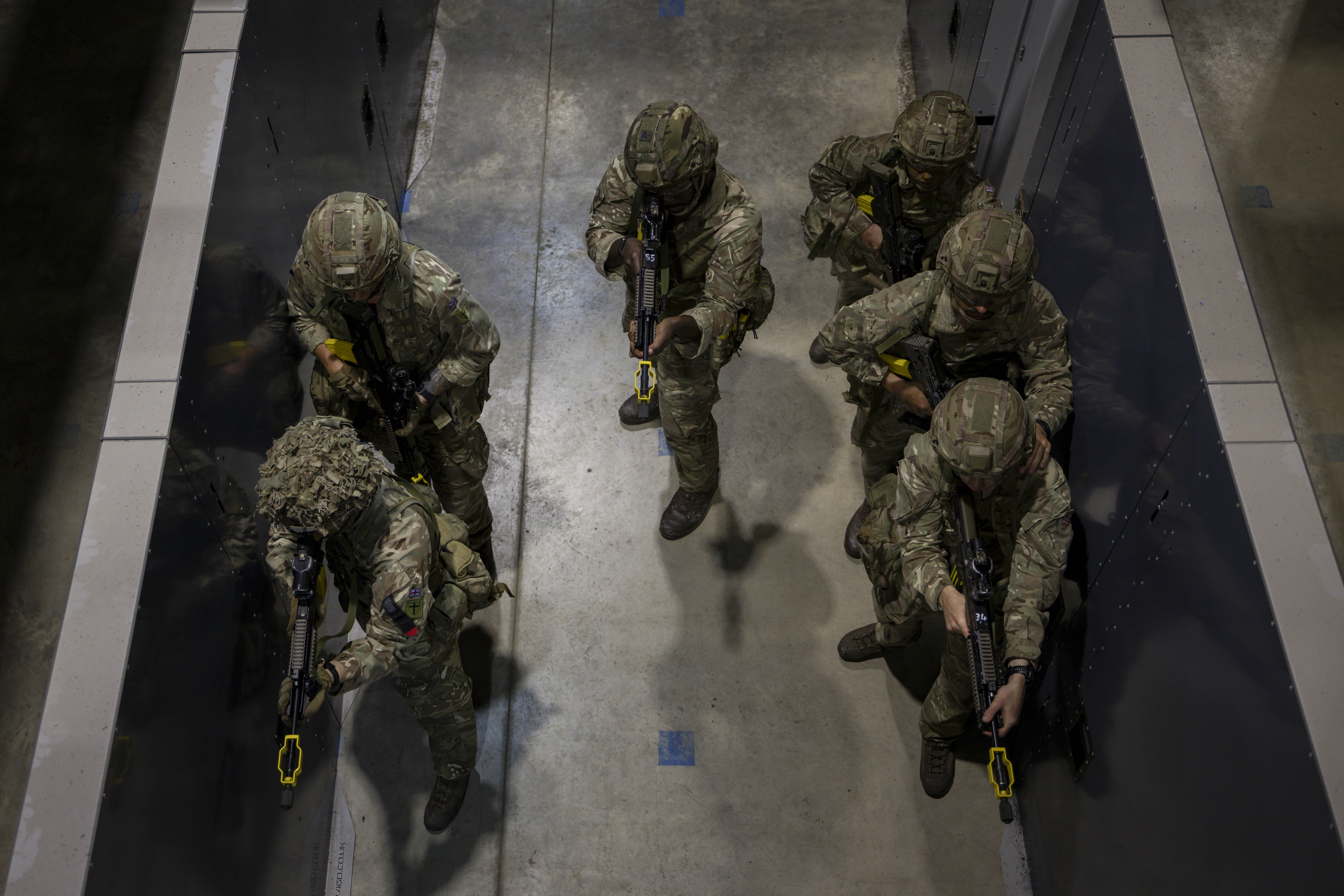 Soldiers in camouflage uniforms holding rifles stand ready in concrete building 