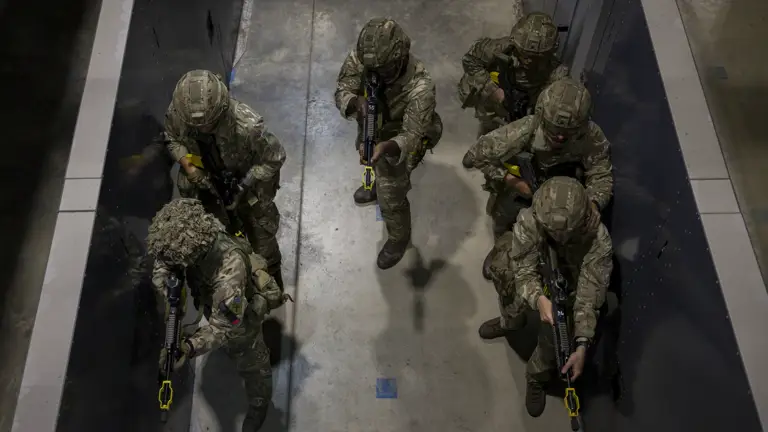 Soldiers in camouflage uniforms holding rifles stand ready in concrete building