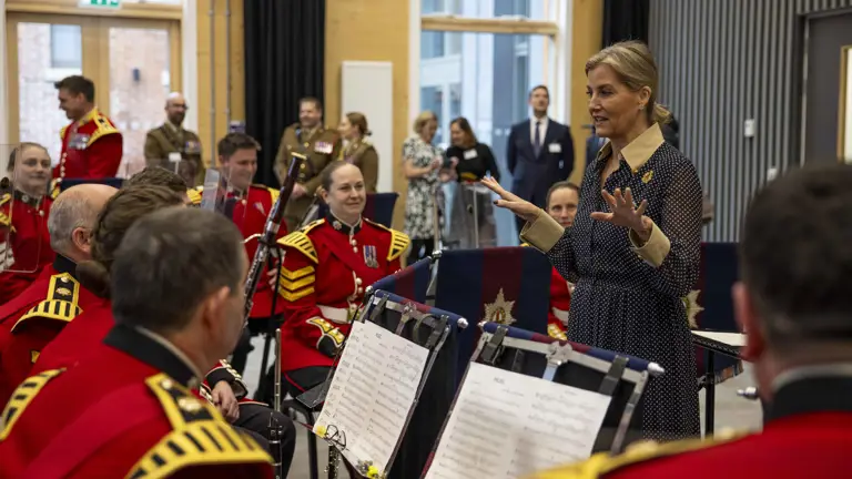 Her Royal Highness, The Duchess of Edinburgh, stands in front of a band of soldiers wearing red tunics and holding musical instruments.