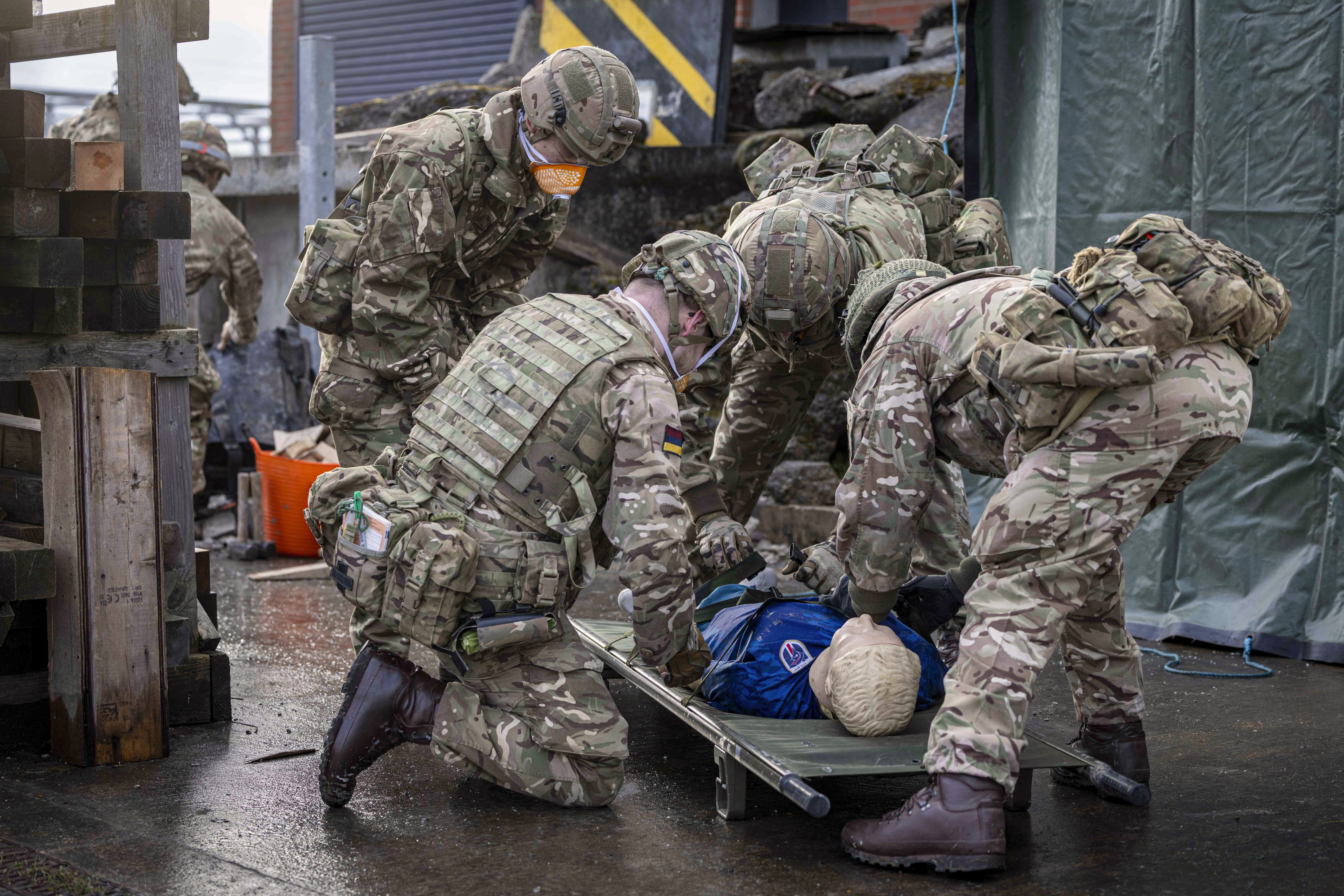 Soldiers in camouflage uniforms perform a medical evacuation drill using a stretcher with a training dummy.