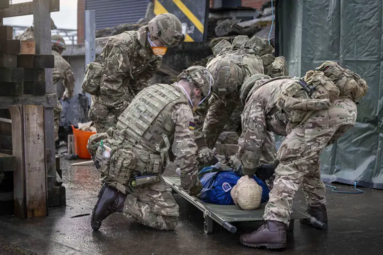 Soldiers in camouflage uniforms perform a medical evacuation drill using a stretcher with a training dummy.