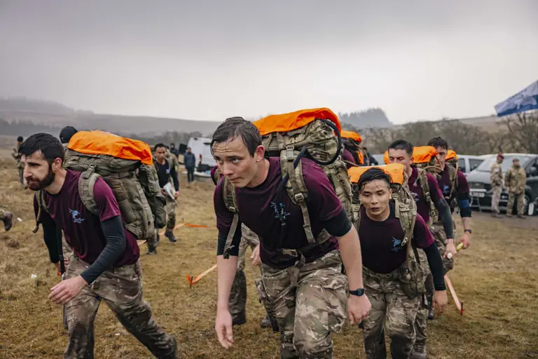 Soldiers from 216 (Para) Signals Squadron team set off to check point 4 during the 40 mile endurance march, wet from the rain and carrying a large green camouflage backpack with their gear.