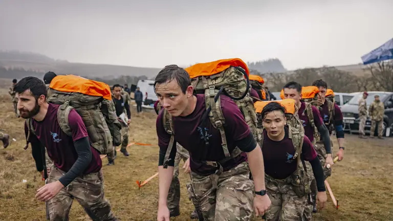 Soldiers from 216 (Para) Signals Squadron team set off to check point 4 during the 40 mile endurance march, wet from the rain and carrying a large green camouflage backpack with their gear.