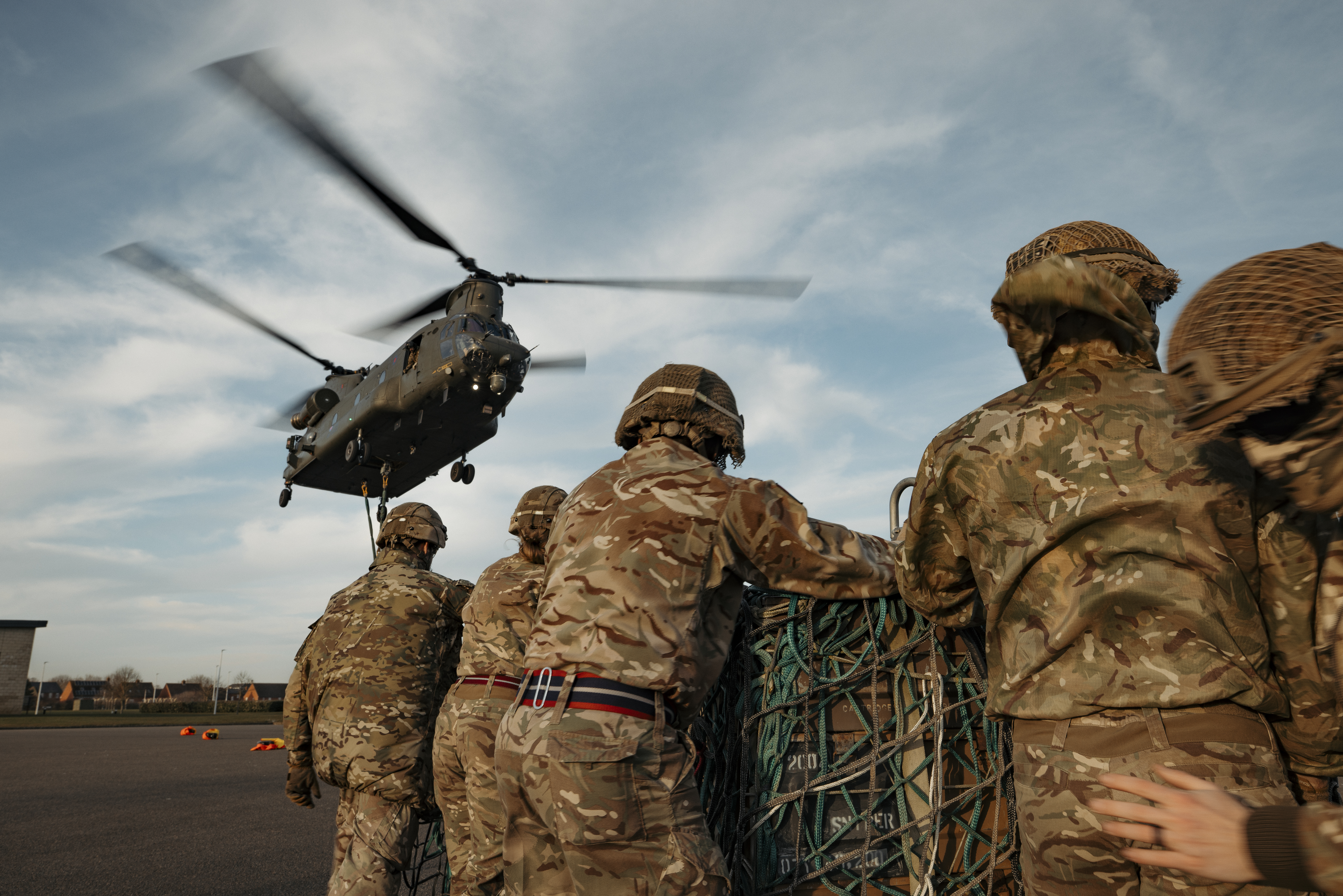 Soldiers wearing their camouflage uniform and helmets stand waiting with a load as a chinook coming into be loaded.