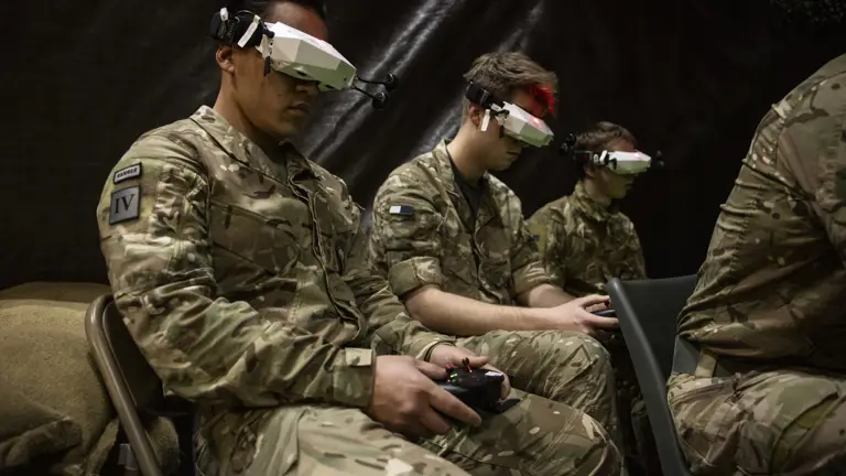 Three men in uniform are pictured with headset technology and controllers.