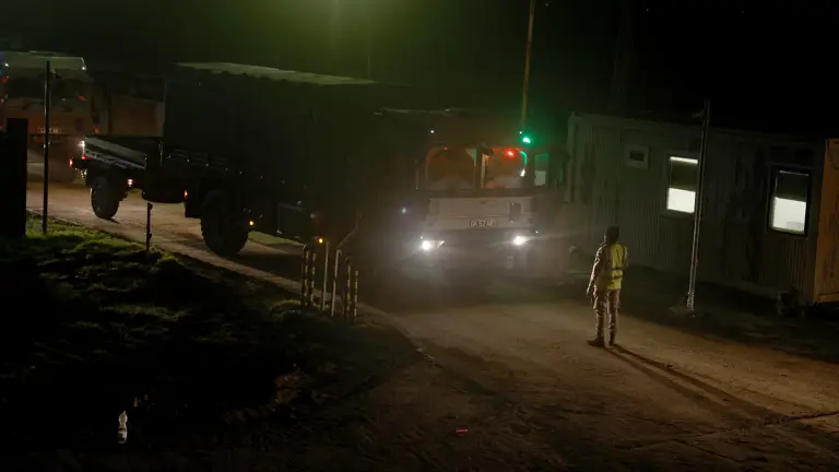 Large army transport vehicle being guided by a soldier in camouflage uniform at night.