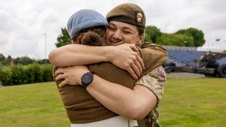 Chloe is photographed in her brown uniform and blue Army Air Corps beret stood next to her mum Sherene who is dressed in her camouflage uniform. They are both smiling and have their arms around each embracing in a hug.