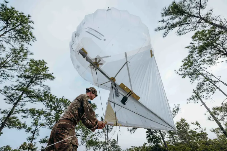 In a jungle environment, a British Army officer is prepared to raise a Helikite (balloon) attached with trail radio equipment to increase the range of the radio frequency.