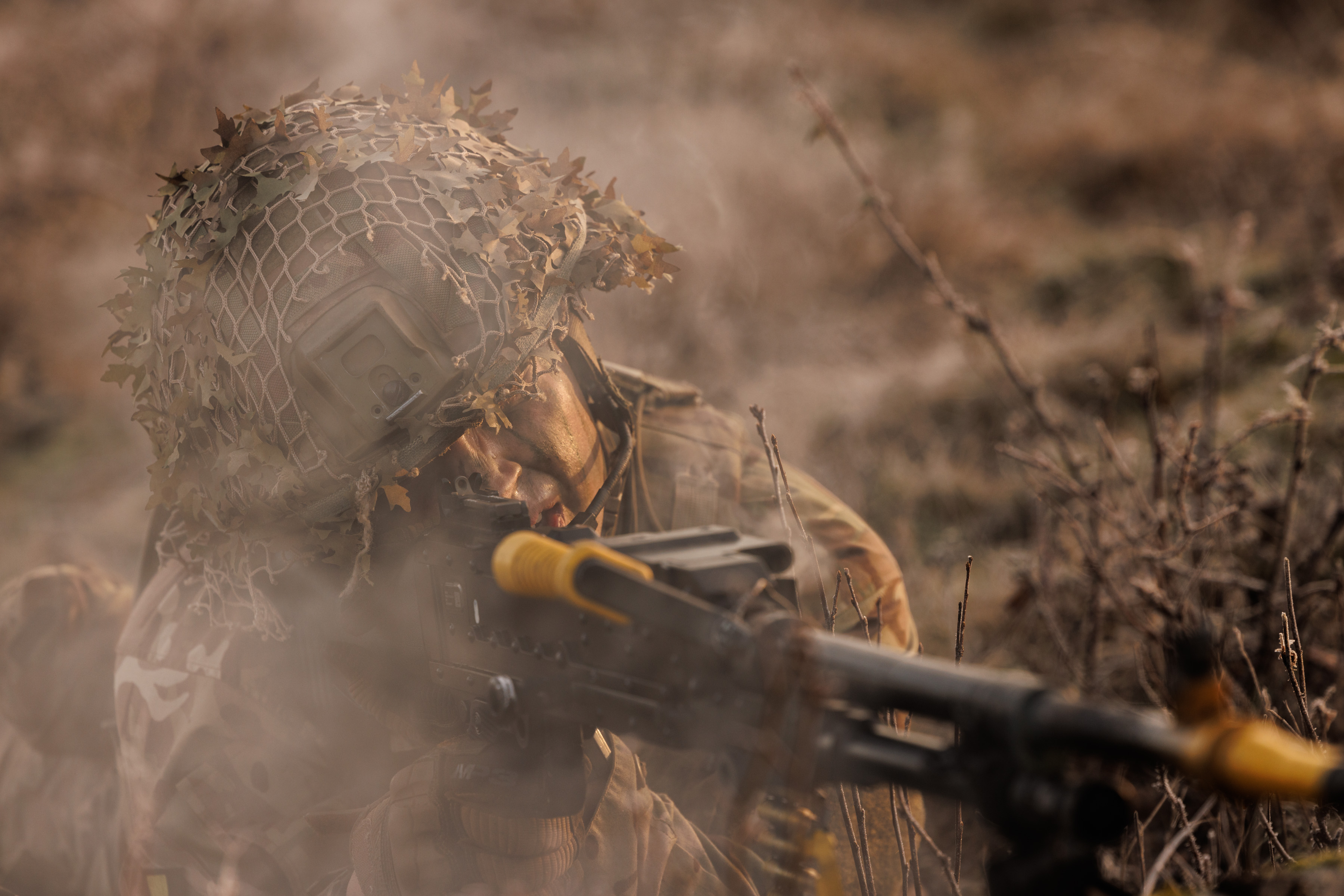 Soldier seen on exercise wearing camouflage uniform, camouflage cream and a helmet shooting a machine gun. 