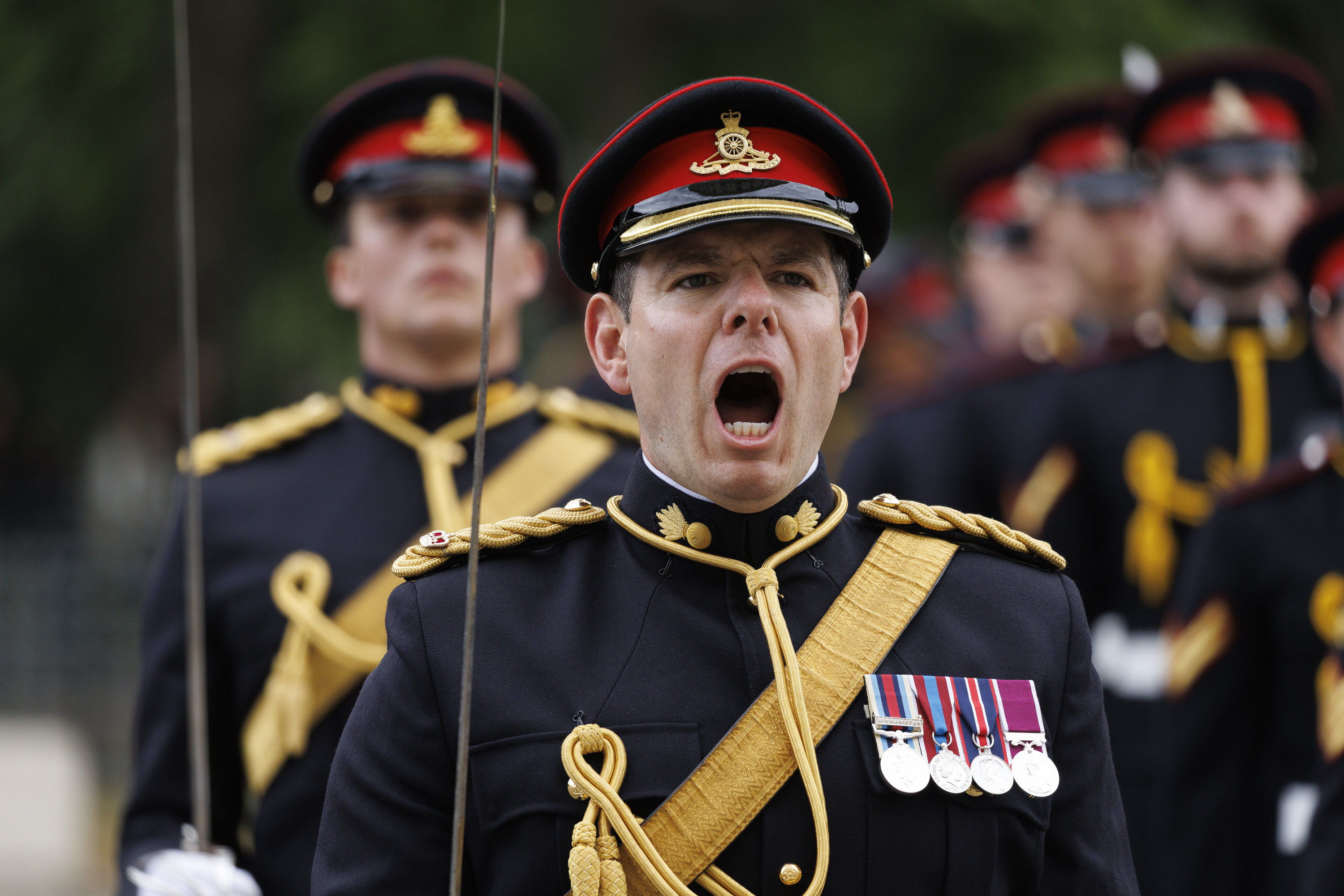 A person in a dress uniform, adorned with multiple medals on the chest, is leading a group of similarly dressed personnel