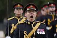 A person in a dress uniform, adorned with multiple medals on the chest, is leading a group of similarly dressed personnel