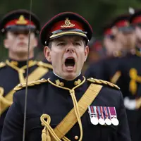 A person in a dress uniform, adorned with multiple medals on the chest, is leading a group of similarly dressed personnel