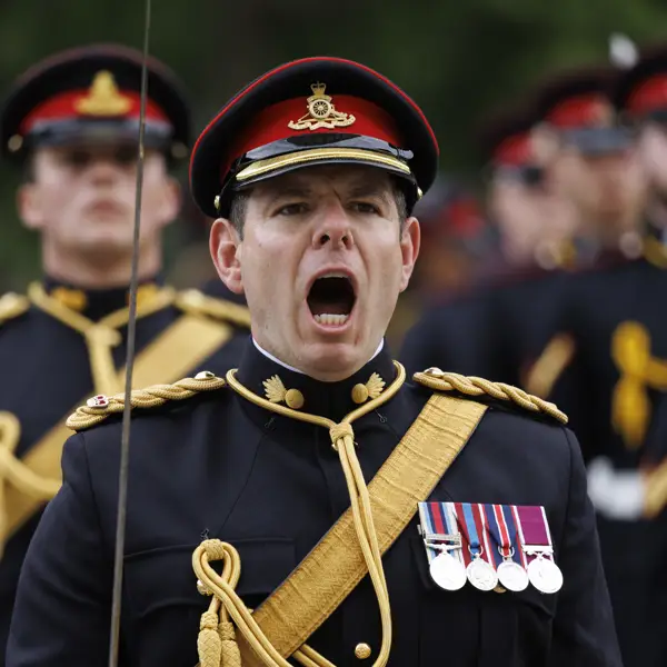 A person in a dress uniform, adorned with multiple medals on the chest, is leading a group of similarly dressed personnel
