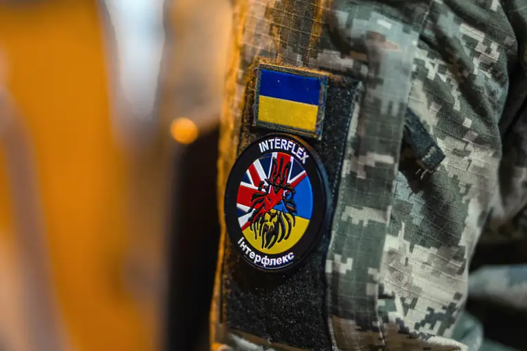A camouflage uniform sleeve with a patch displaying the Ukrainian flag and another patch showing a circular emblem. 