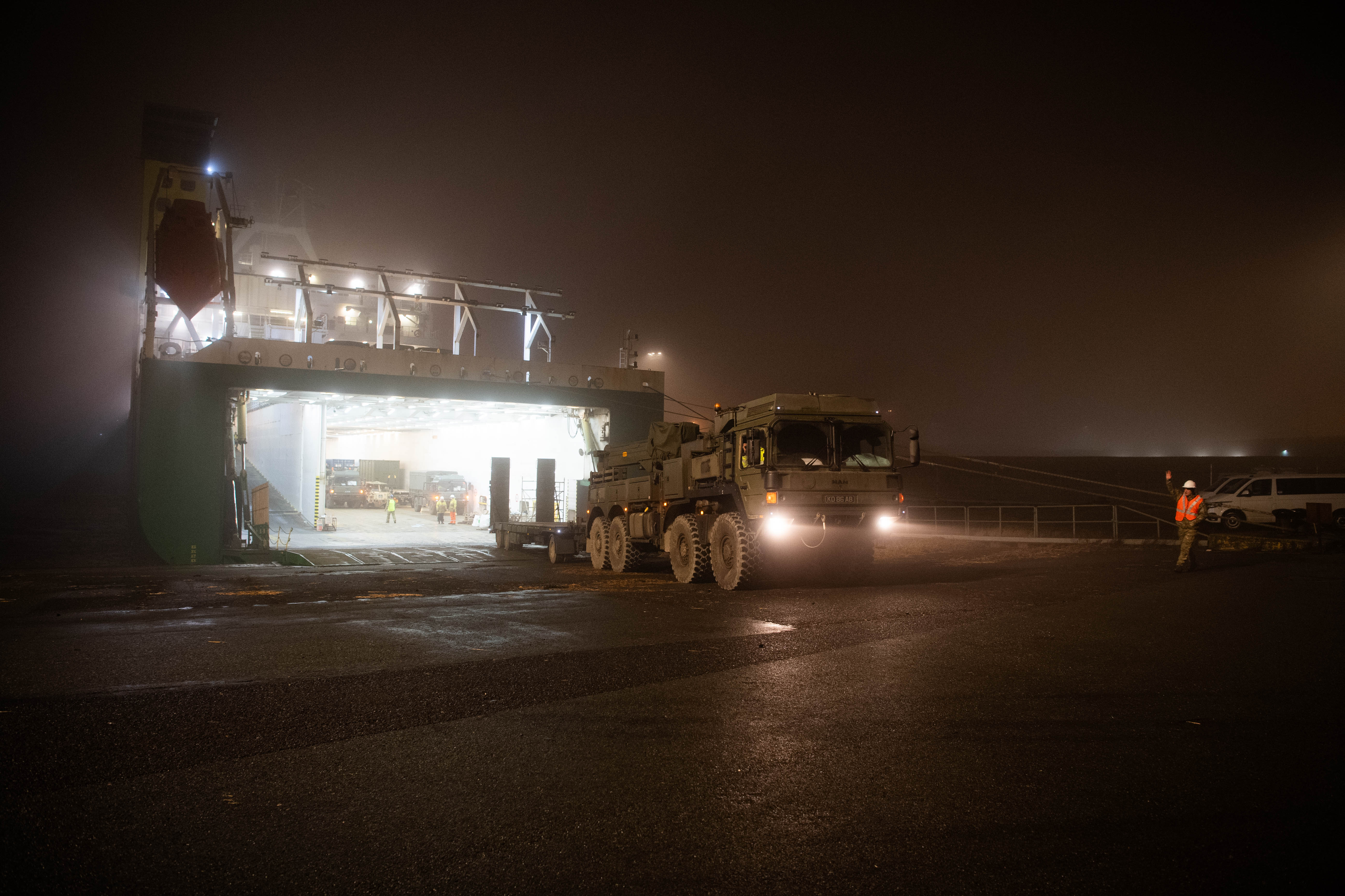 Large military vehicles are seen being directed off the ship after arriving in their new destination at night.