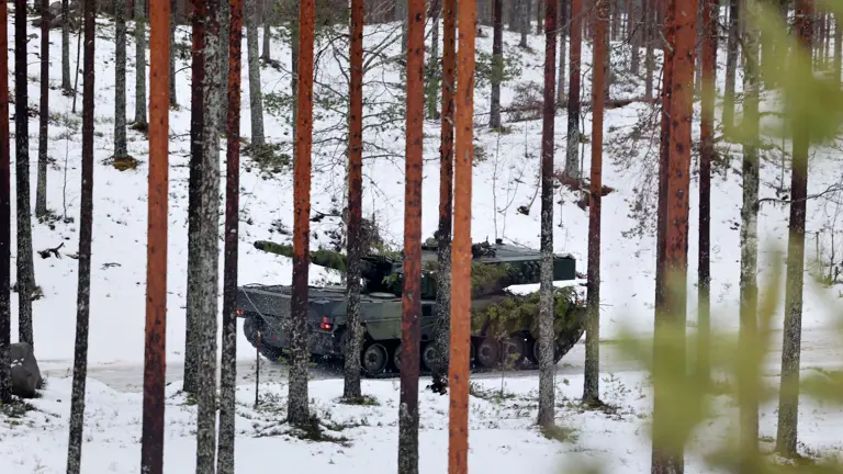 A military vehicle camouflaged with foliage traverses a snowy forest, surrounded by tall pine trees, creating a still, cold, and secretive atmosphere.
