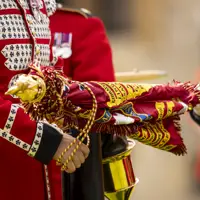 Close-up of a soldier in a red ceremonial uniform holding a decorated regimental flag with gold fringe.