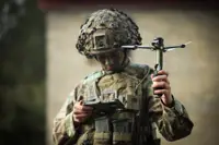 A man in uniform holds a drone and looks down at a portable screen.