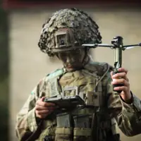 A man in uniform holds a drone and looks down at a portable screen.