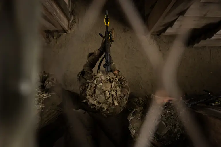 A top down perspective of a soldier walking through the building with his rifle ready, wearing camouflage uniform and a helmet. 