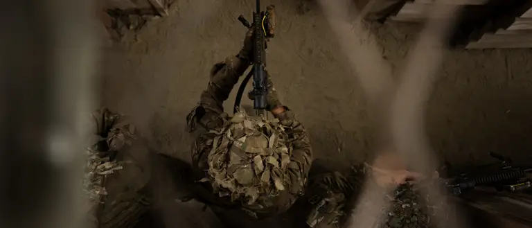 A top down perspective of a soldier walking through the building with his rifle ready, wearing camouflage uniform and a helmet.