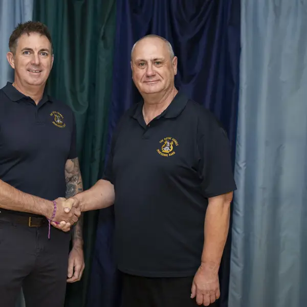 Two people are shaking hands in front of a curtain backdrop. Both are wearing dark polo shirts with embroidered logos.