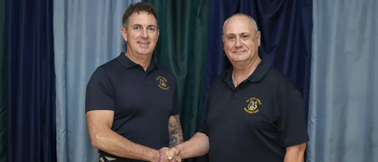 Two people are shaking hands in front of a curtain backdrop. Both are wearing dark polo shirts with embroidered logos.