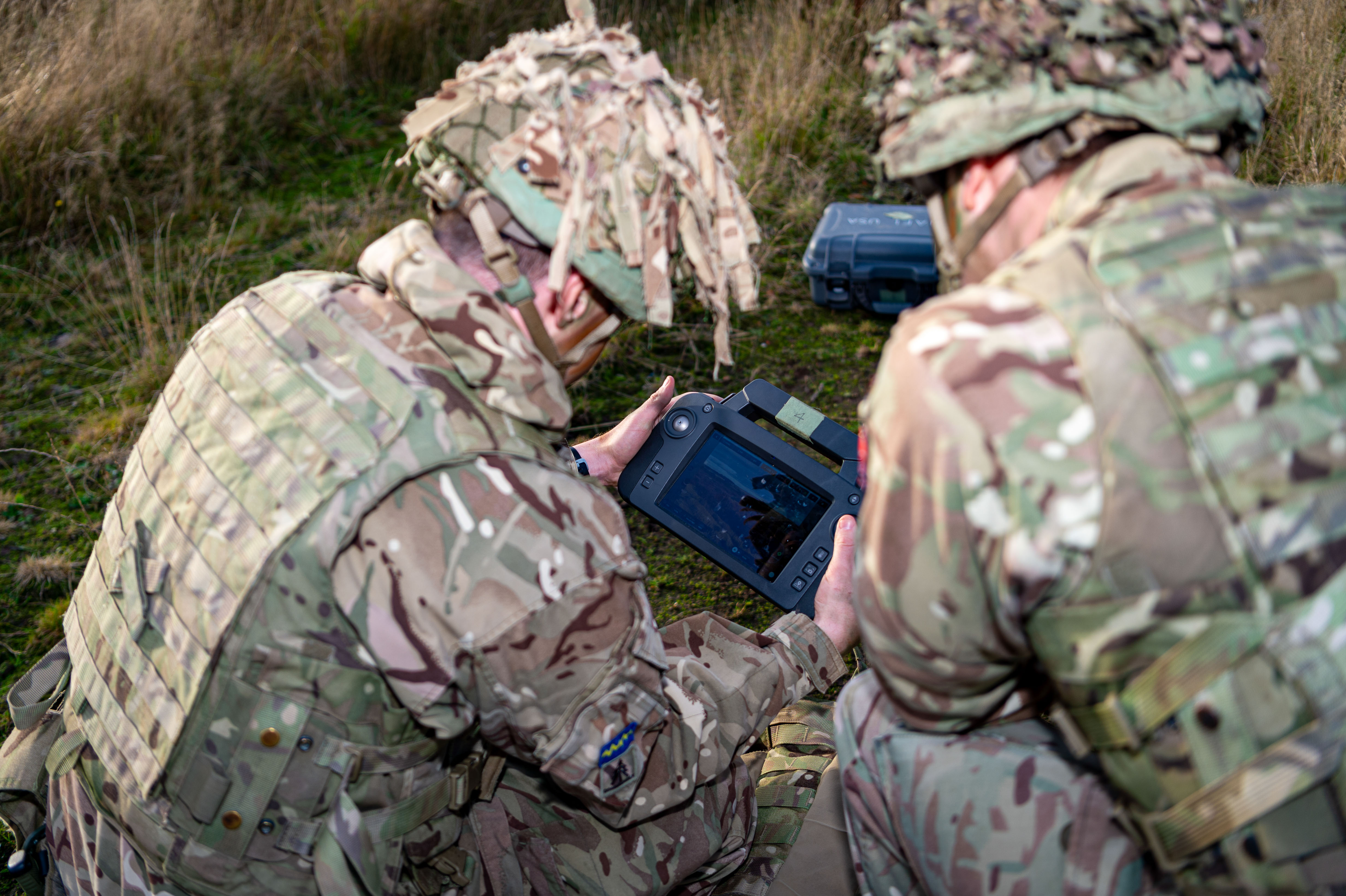 Two personnel in uniform are pictured analysing a computerised device. 
