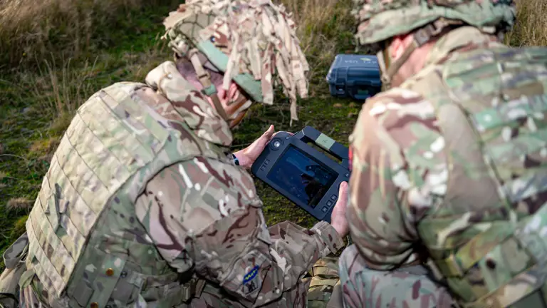 Two personnel in uniform are pictured analysing a computerised device.