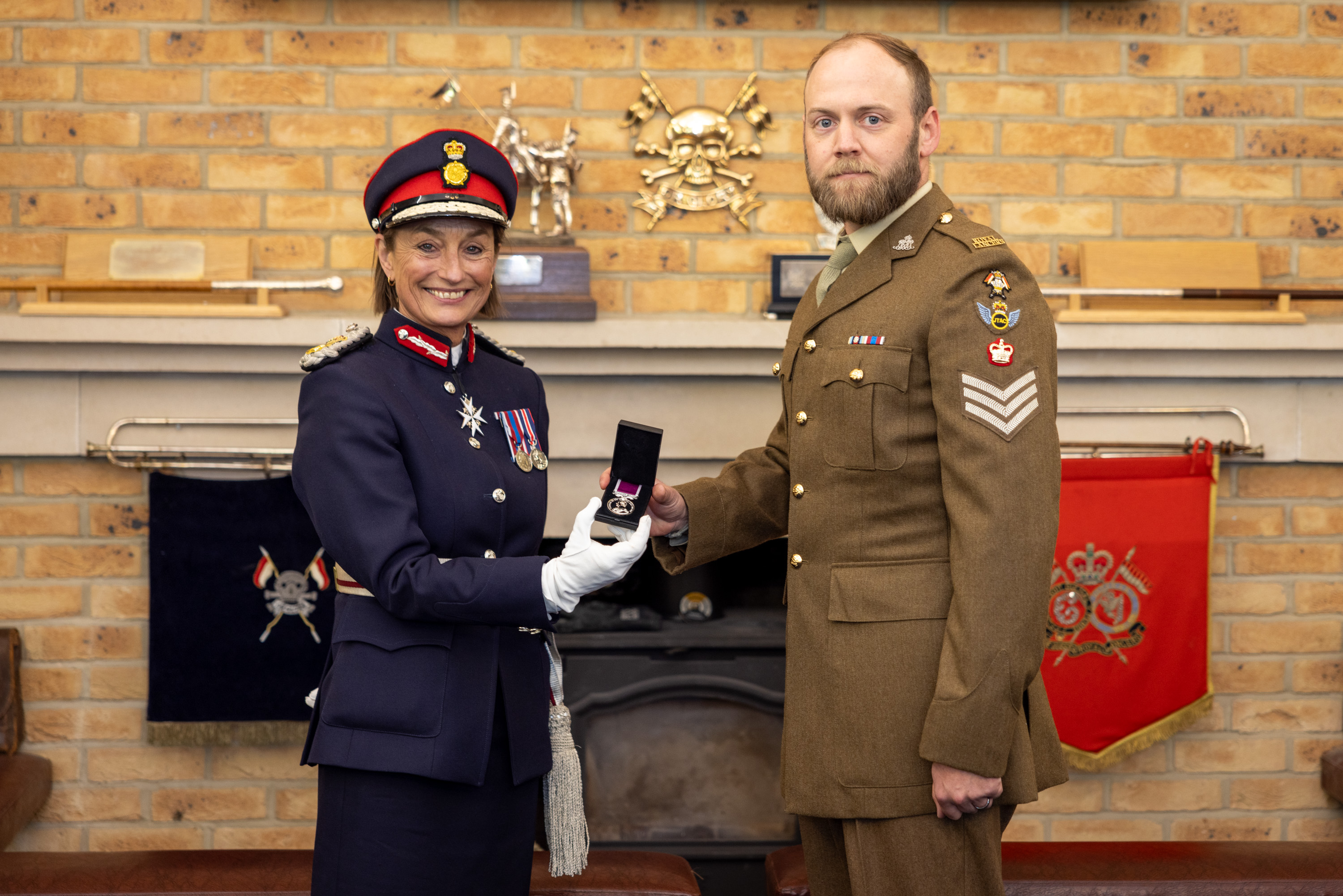 A woman in dark navy ceremonial attire holds up a medal alongside a man in brown ceremonial attire.